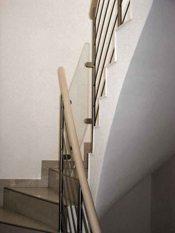 Balustrade rampante type Reling en inox sur escalier béton, avec main courante en bois. Remplissage entre les volées en verre.