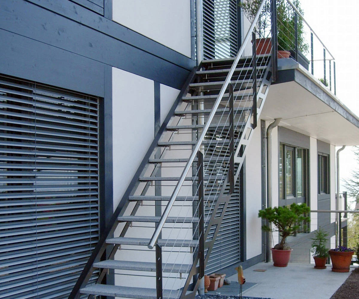 Escalier d'extérieur avec limons métalliques, balustrades montantes avec poteaux en fer T, main courante et câbles en inox. Maches en pierre.