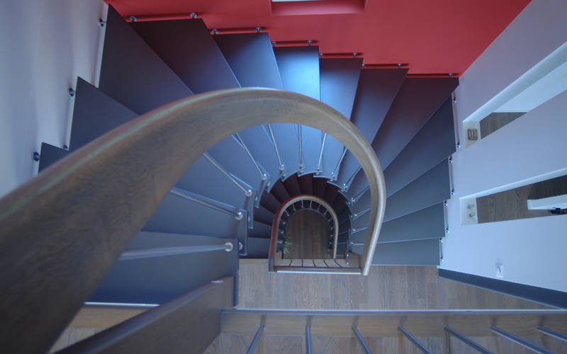 Freitragende halbgewendelte Treppe mit gebogenem Handlauf und Edelstahlsprossen. Stufen farbig deckend versiegelt und Handlauf in Holz.