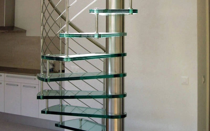 Escalier colimaçon avec marches en verre clair et rampes type Reling, fût central et main courante courbe en inox.