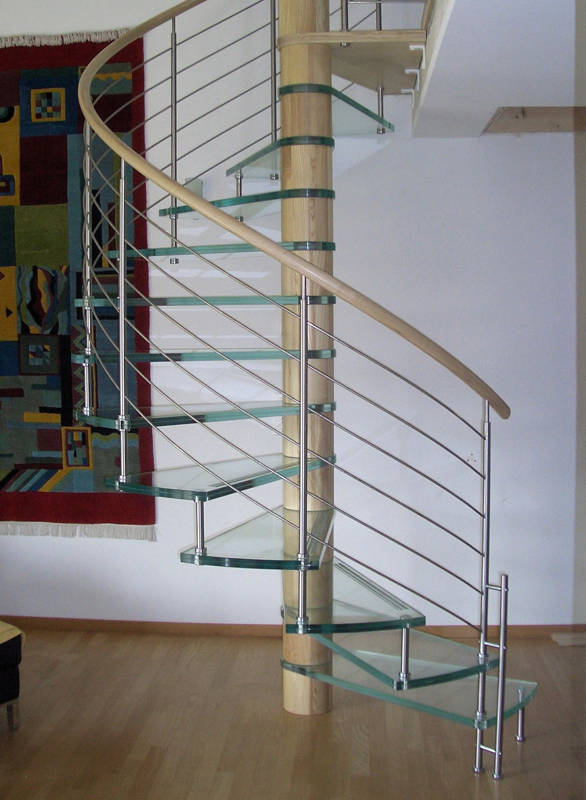Escalier colimaçon avec marches en verre clair et rampes type Reling, fût central en bois et main courante courbe en bois.